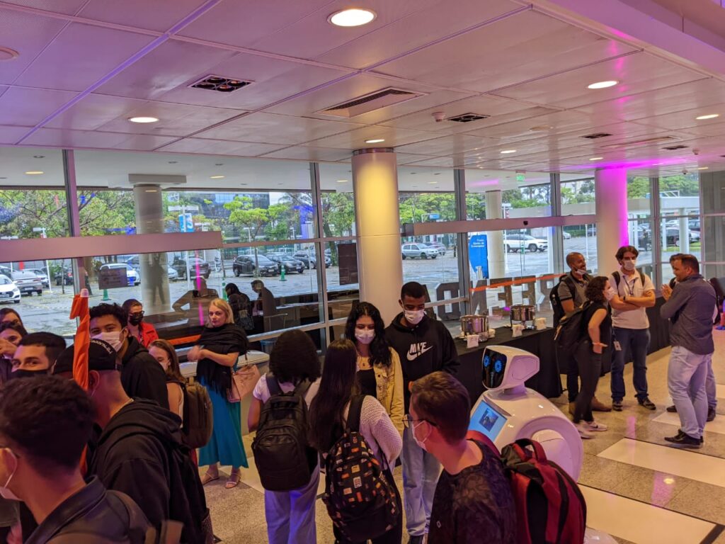 Pessoas interagem com um robô Dubô durante o intervalo de um evento. Exemplo de aluguel de robô para eventos, criando engajamento e networking.